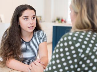 Teenage girl with brown hair in white and blue striped top is talking to an older woman with blonde hair whose back is facing the reader