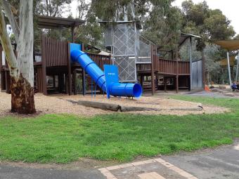 Wooden play structure with enclosed blue slide surrounded by gum trees