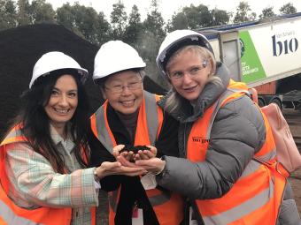 Three Manningham councillors smiling and wearing hard hats, stand holding a handful of compost. In the background is a large pile of compost and a Bio Gro truck.