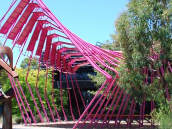 Red metal sculpture in front of a black building surrounded by trees