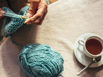 above shot of two hands knitting with a cup of tea