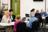 A group of people of mixed ages, ethnicities and genders sit around tables talking.