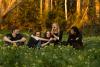 Members of the band BOTH sitting in a field of grass and yellow flowers with bushland in the background.