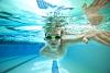 A young boy with goggles on swimming underwater in a large swimming pool