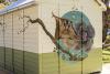A mural of a sugar glider possum, a tree branch and a cabbage looking plant on a yellow and green painted timber shed.